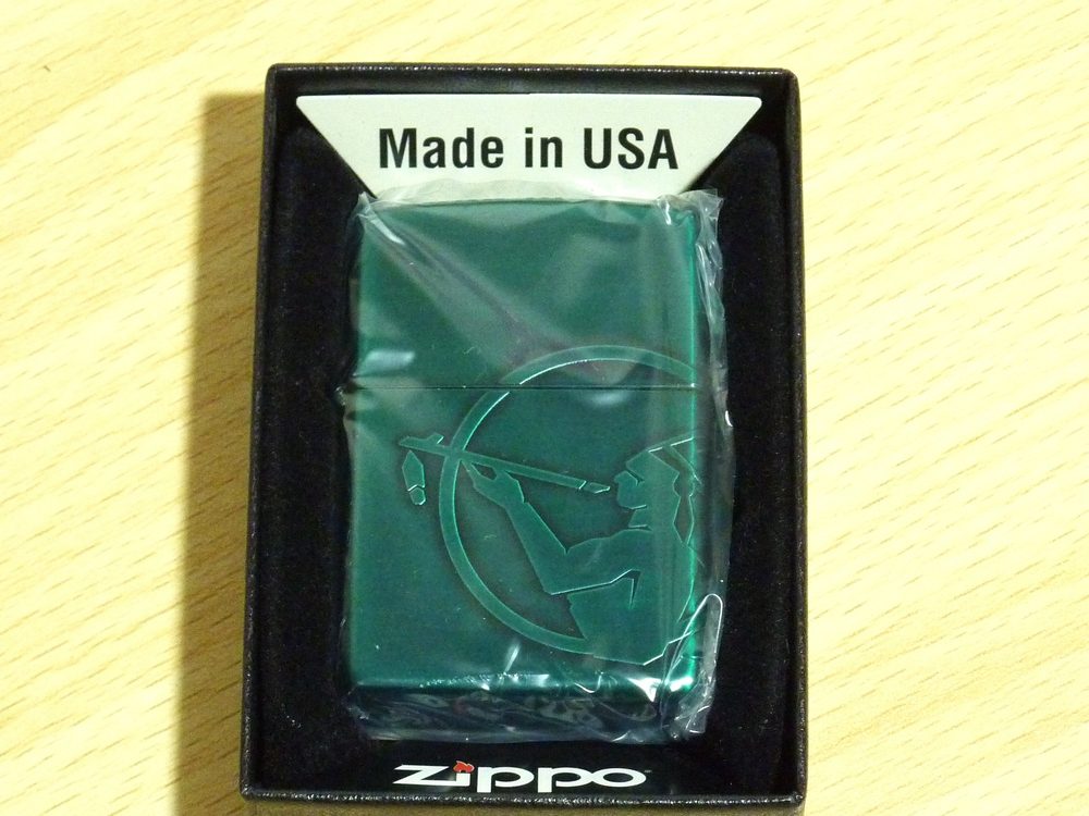 袋に包まれたまま箱に入ったZIPPO。緑色の本体に、丸い枠の中でパイプをくわえた人物の図柄